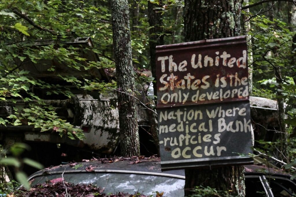 A brown wooden sign attached to tree says, “The United States is the only developed nation where medical bankruptcies occur.”