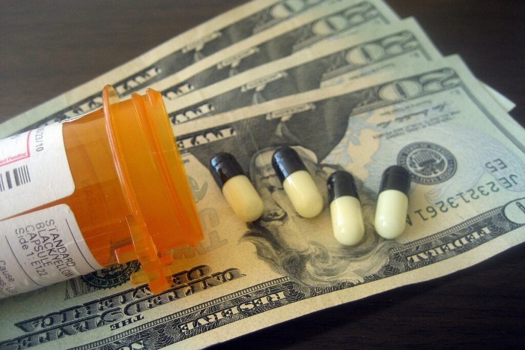 A prescription bottle on the left is atop four $20 bills. Four black and white capsules are atop the money.