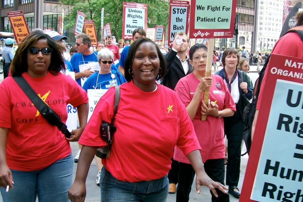Nurses march in the streets. One holds a sign saying “Union Rigths=Human Rights.” Another says, “We fight for patient care.”