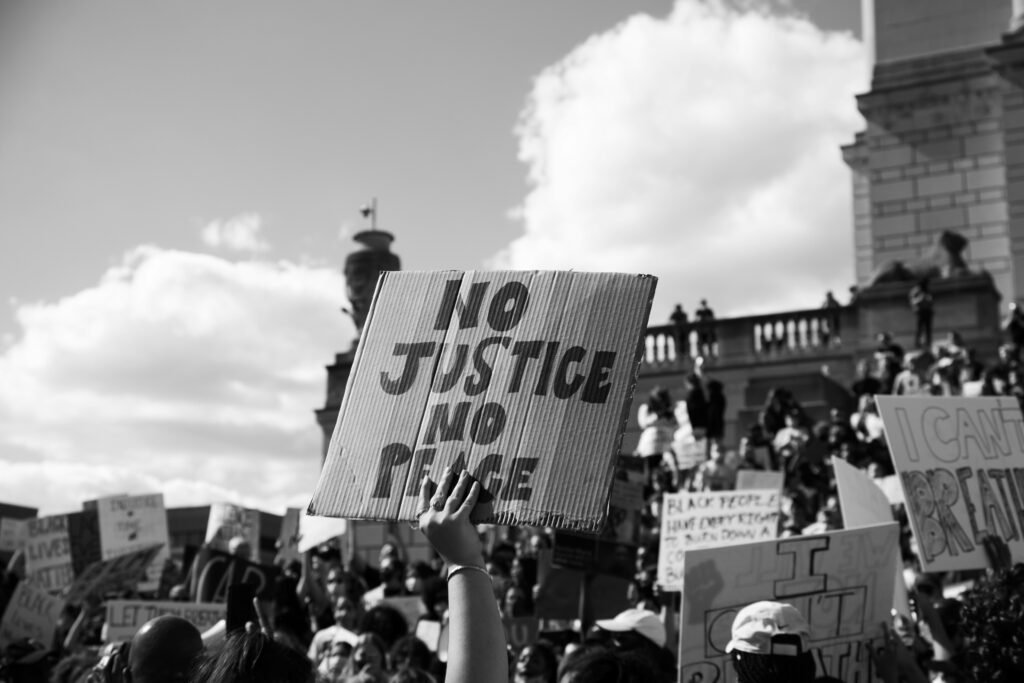 During a protest, a person holds up a cardboard sign that reads, “No Justice No Peace.”