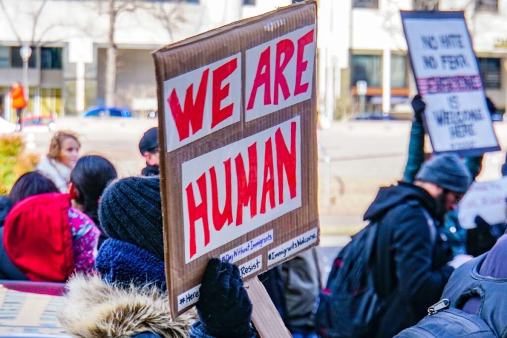 At an immigrant rights rally on an obviously cold day, a cardboard sign says in bright red capital letters, “WE ARE HUMAN.”