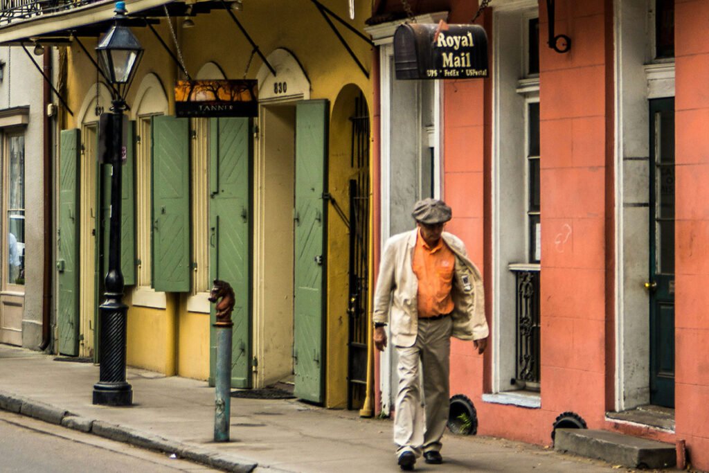 A man walks alone down a rebuilt street in New Orleans in front of pastel colored buildings, symbolizing community led rebuilding and reclamation of space.