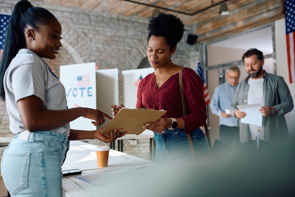 A Black woman with a ponytail helps another woman with on-the-spot voter registration, a practice that will be stripped away with Trump’s new policy.