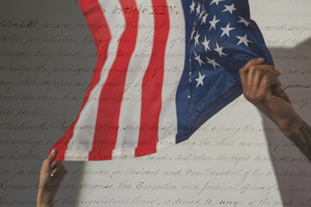 A White woman and Black man’s hand holding the corners of an American flag with the constitution’s 14th amendment superimposed over the image.