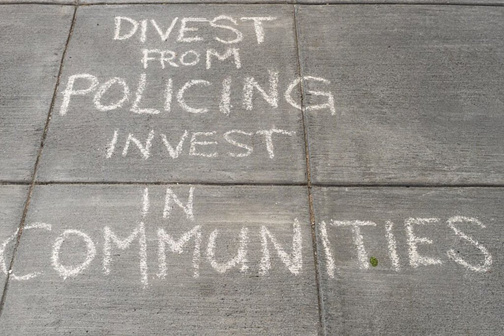 A chalk sign reading “Divest from policing. Invest in communities.”