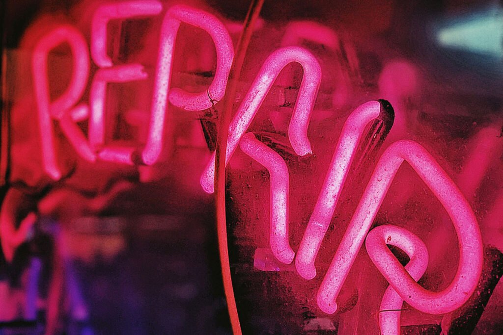 A neon-sign that says “repair” symbolizing the need to confront and self-correct the harms the sector has committed.
