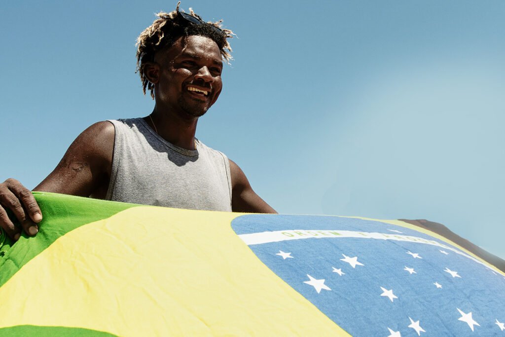 A afro-Brazilian man waving a Brazilian flag joyfully, symbolizing the positive effect that direct funding can have on communities.