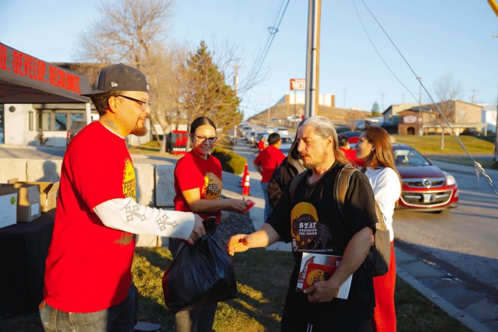 A group of people in red shirts stand outside, handing bags of food out to others.