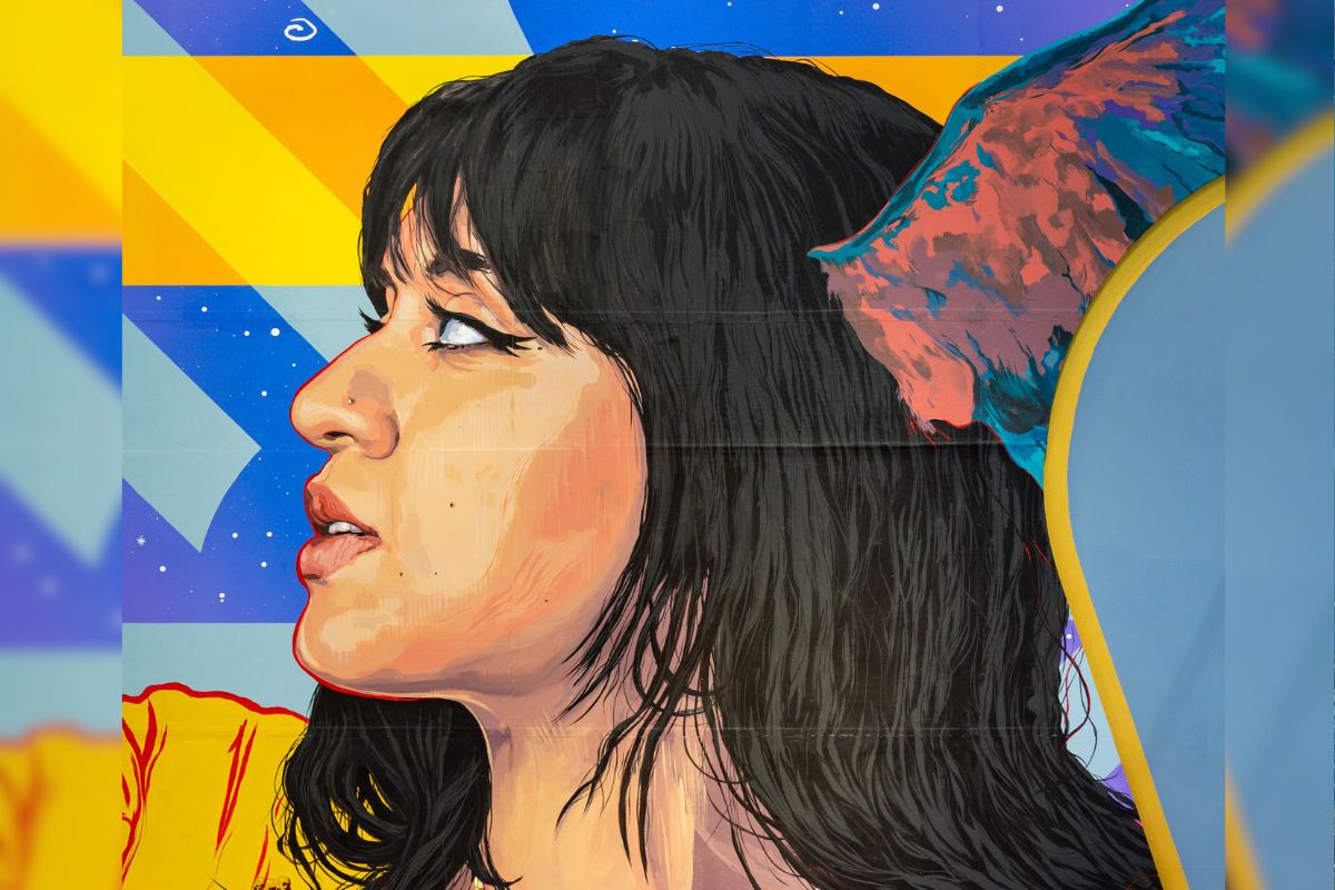 Mural of a woman looking left, wearing a gold necklace with the word “Newark,” overlaid with city buildings and a starry sky in the background.
