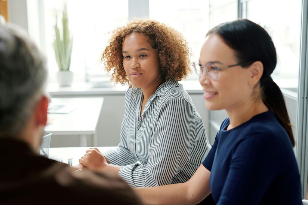 A diverse group of people sit at a table, discussing something together.