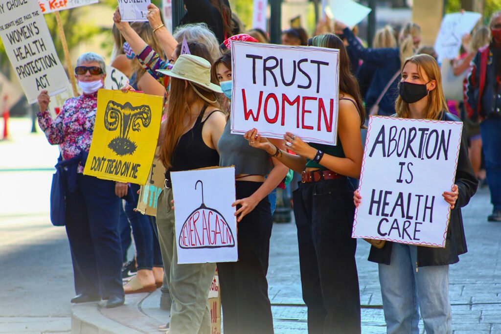 A group of women holding up pro-choice signs that read “trust women”, “abortion is healthcare” and “don’t tread on me”
