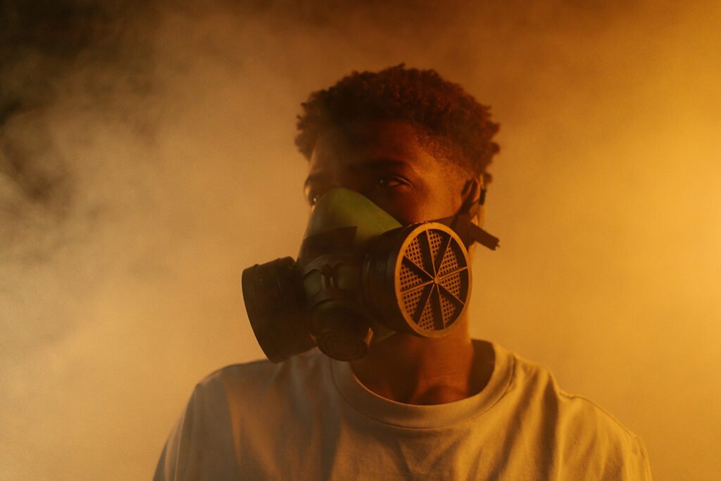A Black man wears a gas mask with plume of brown smoke billowing around him.