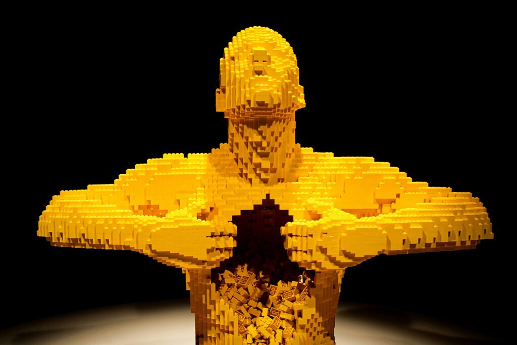 A man made of yellow legos pulling at his chest and opening it up, representing leaders who continue bold thinking even while navigating urgent challenges.