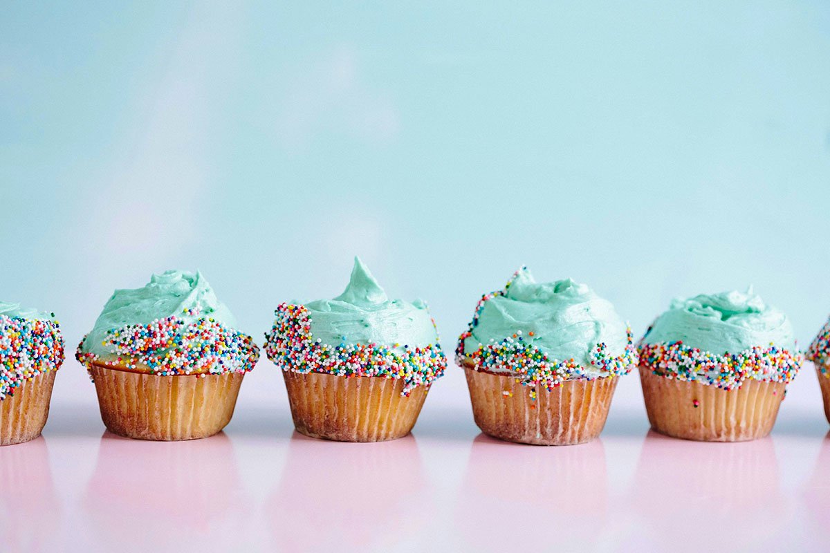 A row of blue, frosted cupcakes with rainbow sprinkles.