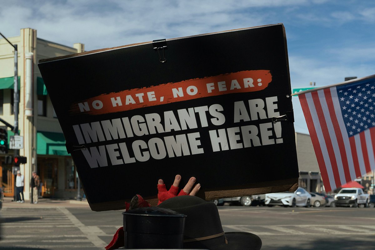 A person’s hand holding up a sign that reads, “No Hate, No Fear: Immigrants are welcome here!”