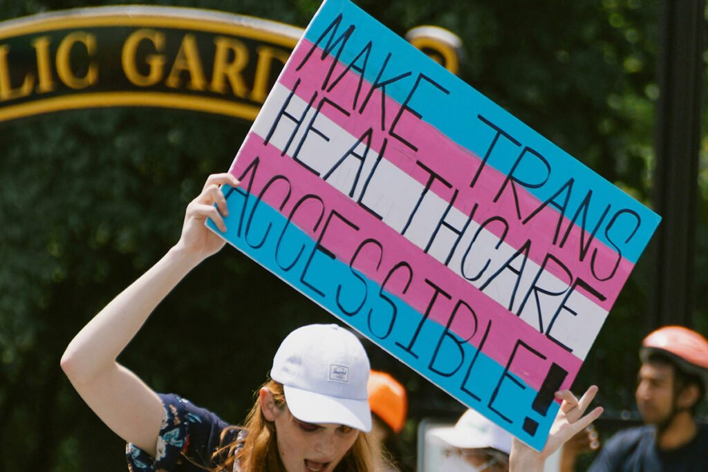 A person holding up a hand-painted sign reading, “Make Trans Healthcare Accessible”