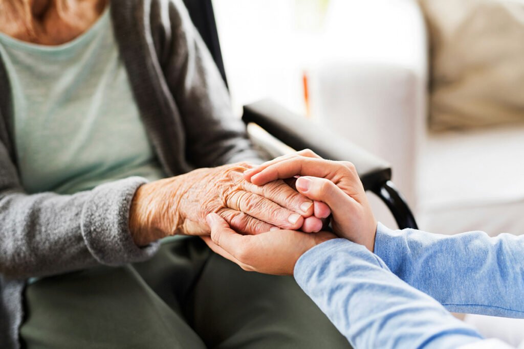 A pair of young hands cradling an elderly hand belonging to a woman in a wheelchair.