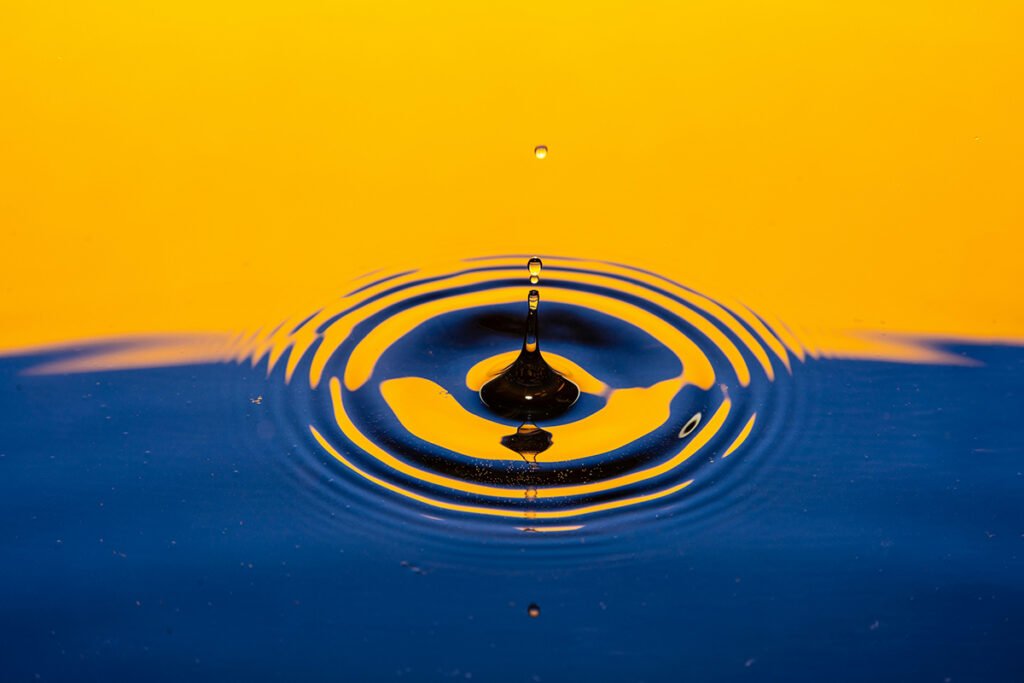 A blue and yellow colorized image of a drop in a body of water, symbolizing the difference charitable giving makes when wealth is not redistributed.