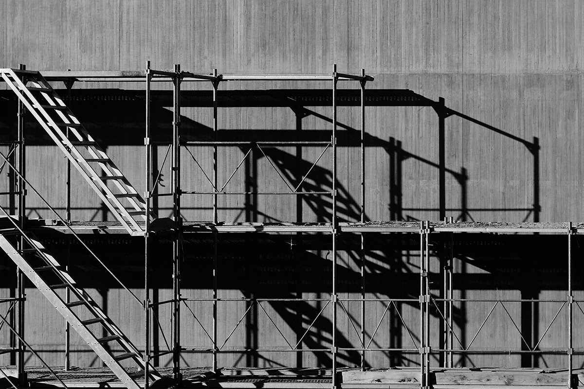 A black and white photo of construction scaffolding leaning against a building, symbolizing the scaffolding and infrastucture needed to sustain movements.