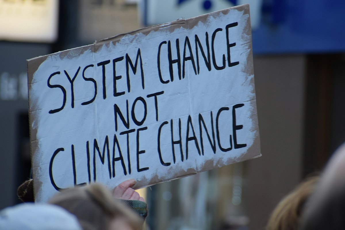 A person holding up a sign that reads, “System Change, Not Climate Change”