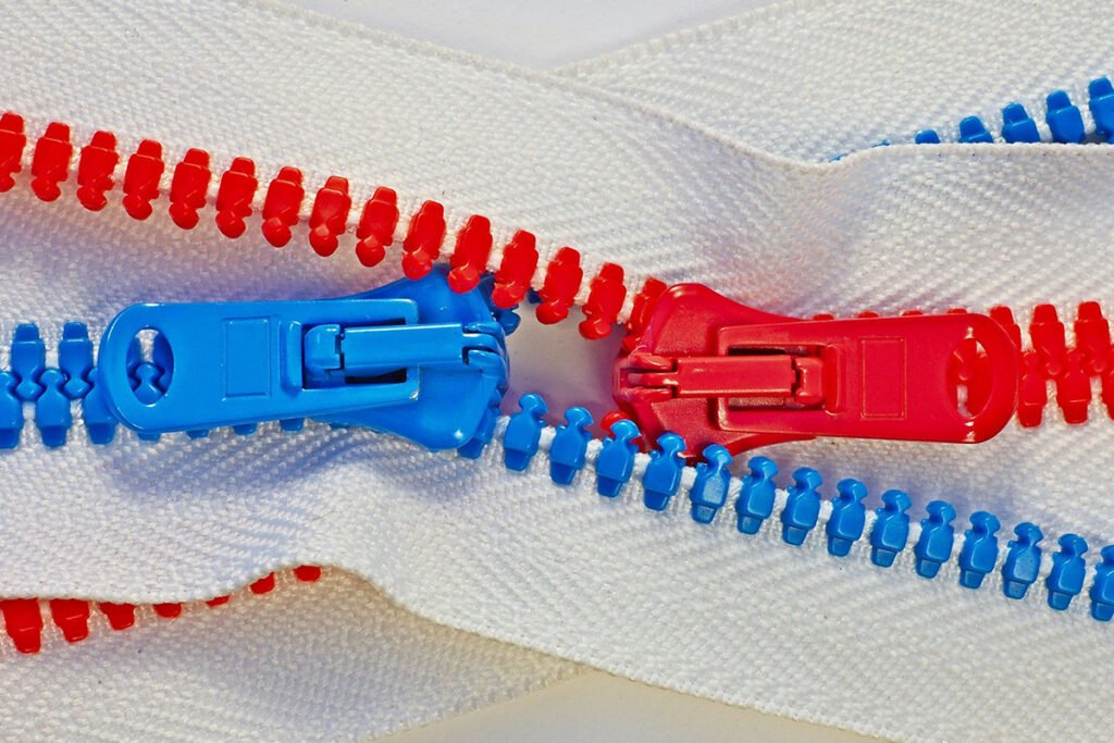 A pair of red and blue zippers, with tracks intertwined to reveal a small gap in between them. Where one zipper stops, the other zipper starts.