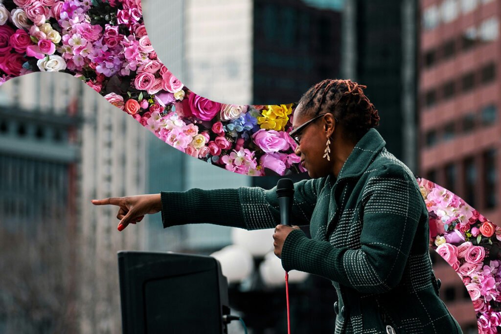 A Black woman local politician in Denver speaks at a rally, with her arm extended charismatically in a pointing position. A band of colorful flowers is superimposed behind her in a flowing motion.