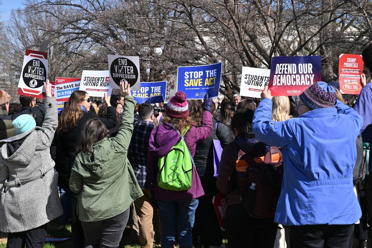 A crowd of people hold signs that read "Stop the SAVE Act", "End Voter Suppression" and "Defend Our Democracy"