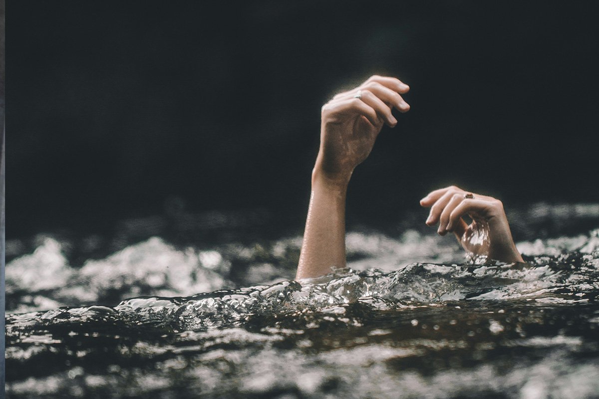 A woman’s hands emerge from a body of water, signifying she is drowning.