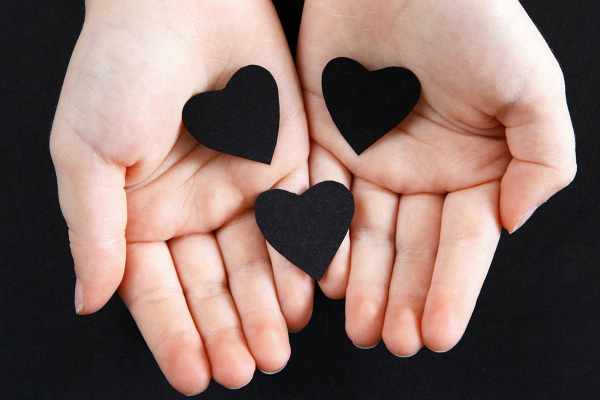 A pair of hands facing palms-up with three black paper hearts in the palms.