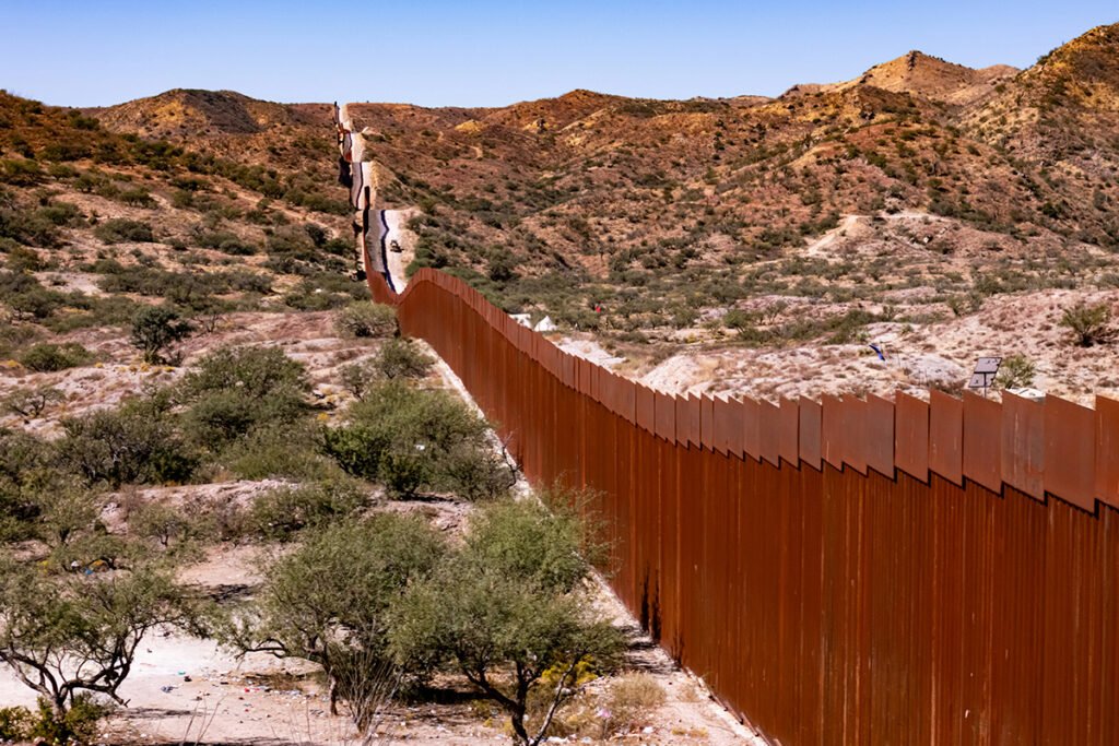 A metal slatted wall at the Mexico-United States border, against a desert landscape.