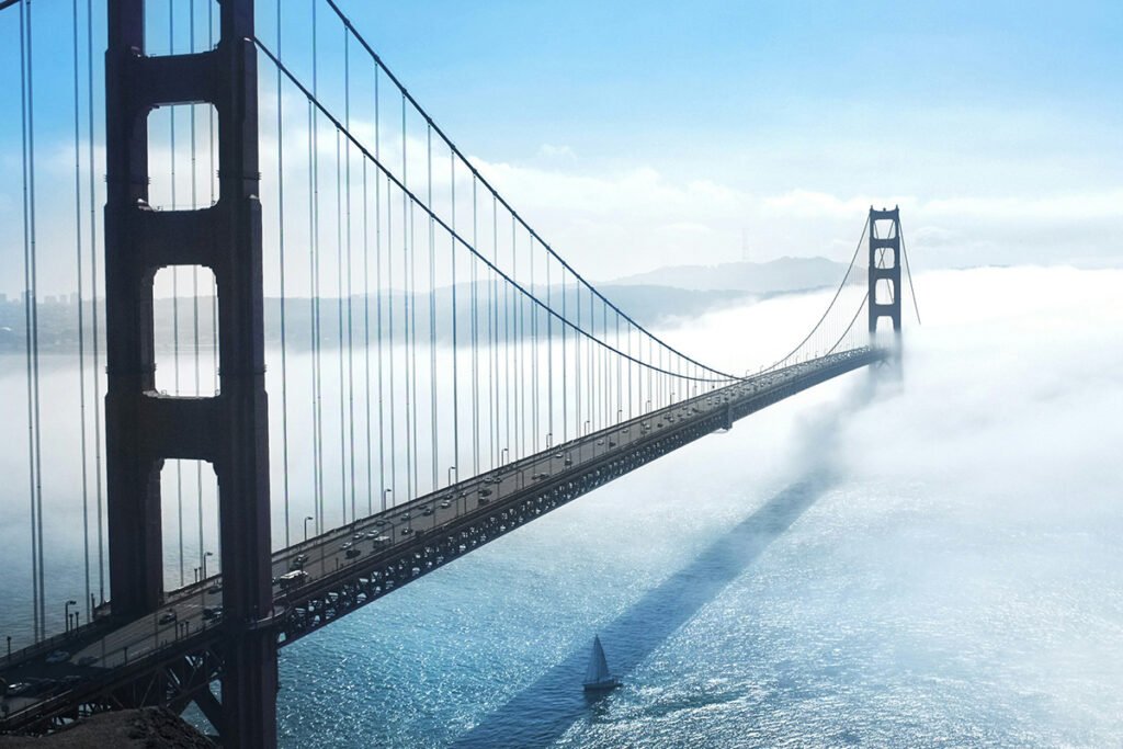 A large suspension bridge reaching out over a body of water, with one end covered in fog.