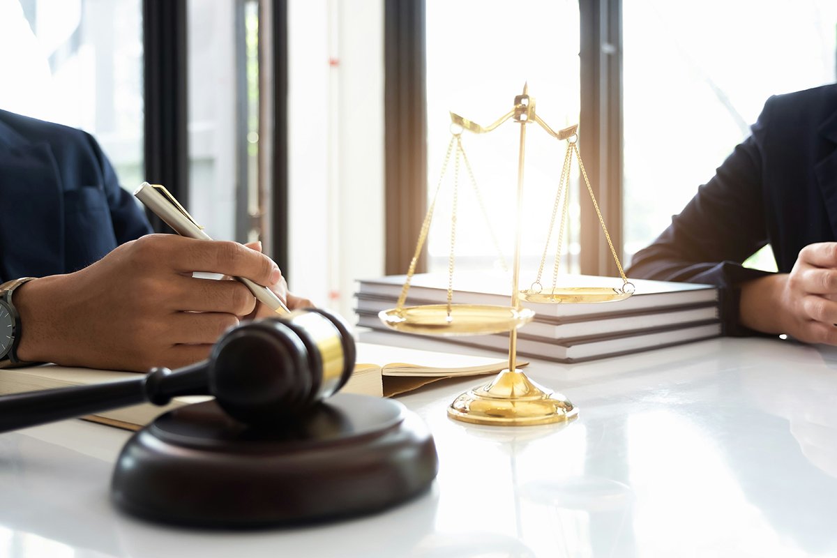 A close-up shot of a lawyer consulting at a table with a client. A golden scale and gavel are placed on the table.