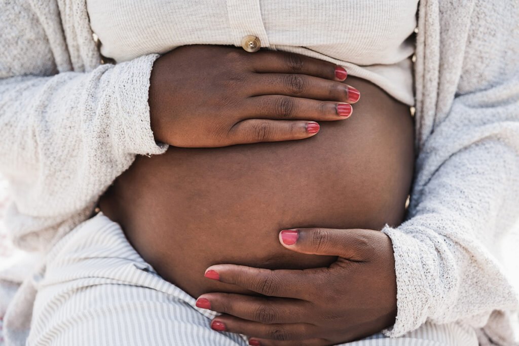 A close up of a Black woman with red painted nails cradling her pregnant belly.