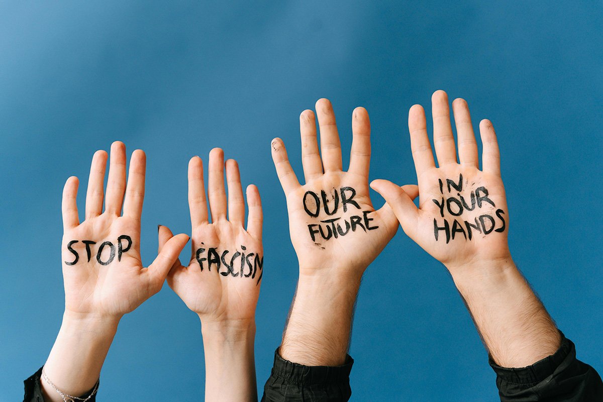 Two pairs of hands raise open-palmed in the air, painted with the words, “Stop Facism, Our Future is in Your Hands”