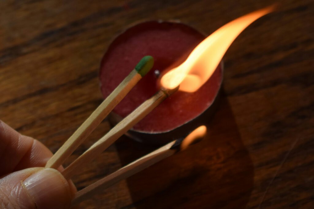 A person’s hand holding three matches, an unlit match, a lot match, and a smoking burned-out match. The relit match is lighting a candle.