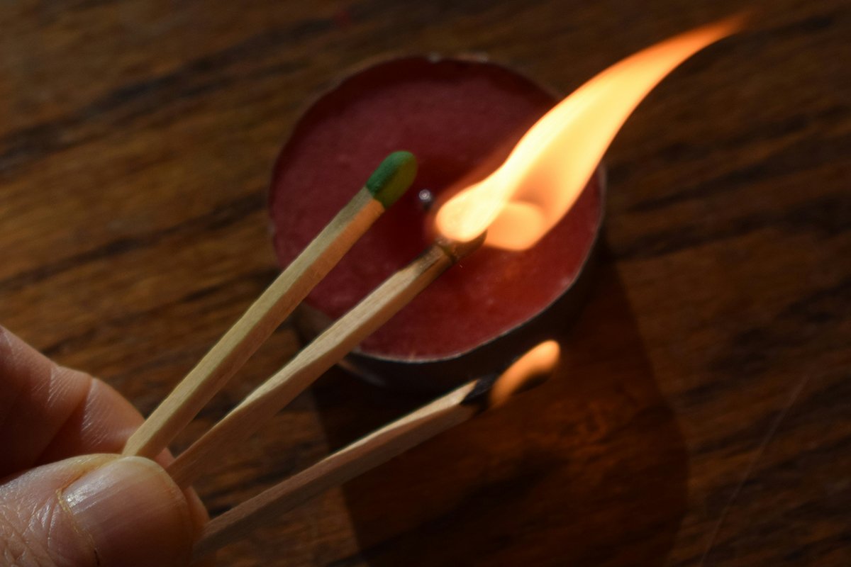 A person’s hand holding three matches, an unlit match, a lot match, and a smoking burned-out match. The relit match is lighting a candle.