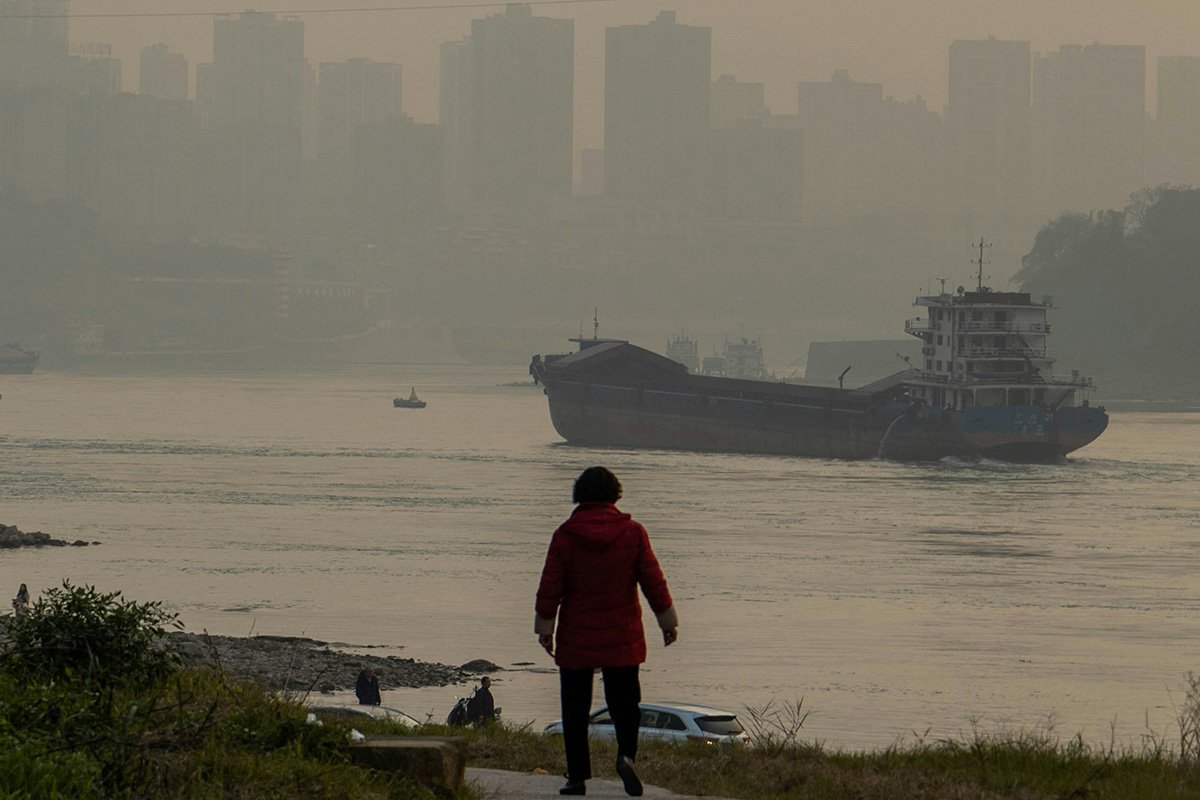 A man in Chongqing, China looks out over a river through a thick brown haze of air pollution.