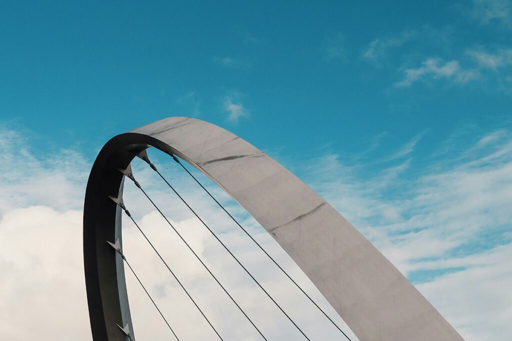 The metal arc of a bridge with suspension supports against a cloudy sky. Elizabeth Quay Bridge, Australia.