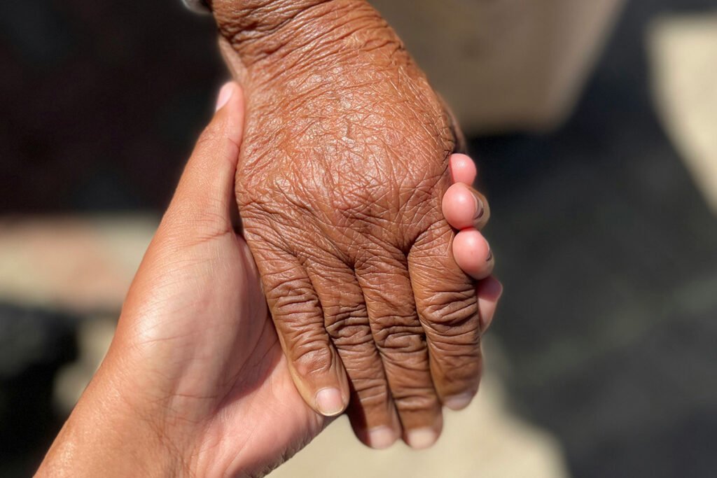 A young persons hands holding onto an elderly person’s hand across a wooden table.