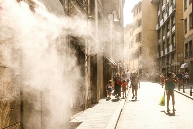 People walk down a hot city street through misting spray.