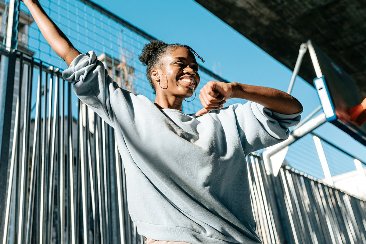 A young, Black girl with an afro puff dancing and smiling broadly at an urban basketball court.
