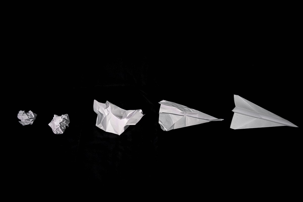 A series of five paper airplanes that start as a crumpled piece of paper and gradually straighten out to a flight-worthy paper airplane.