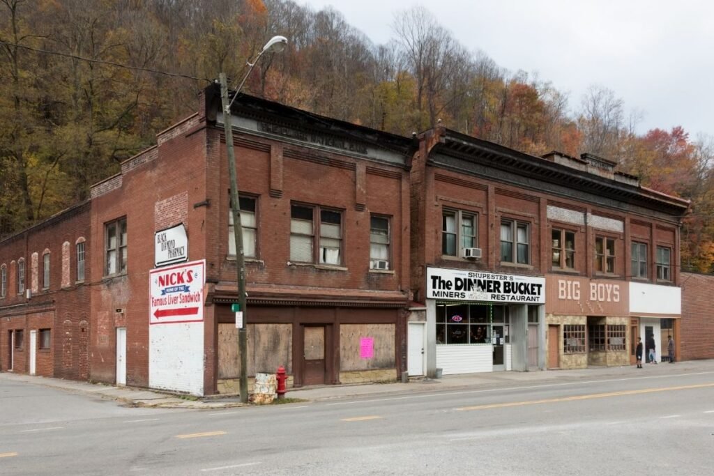 Brick storefronts line an empty street in the Appalachian town of Northfork, West Virginia, some businesses still open, others boarded up, with fall color on the surrounding hills.
