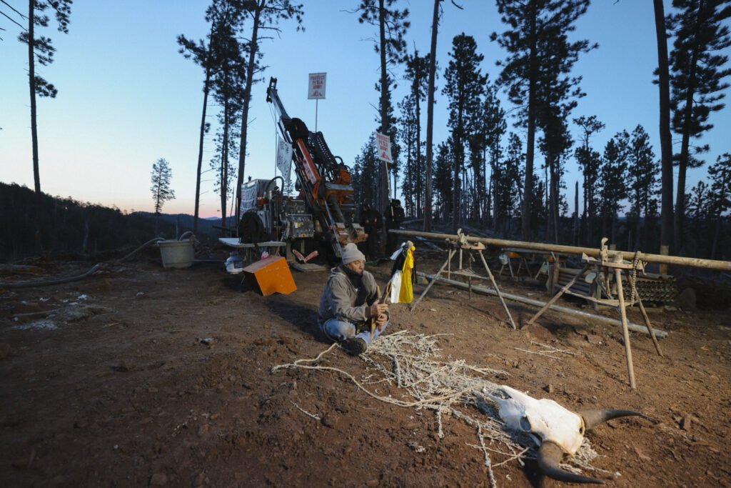 A lone Indigenous man sits in protest of the mining of the sacred site Pe’Sla.