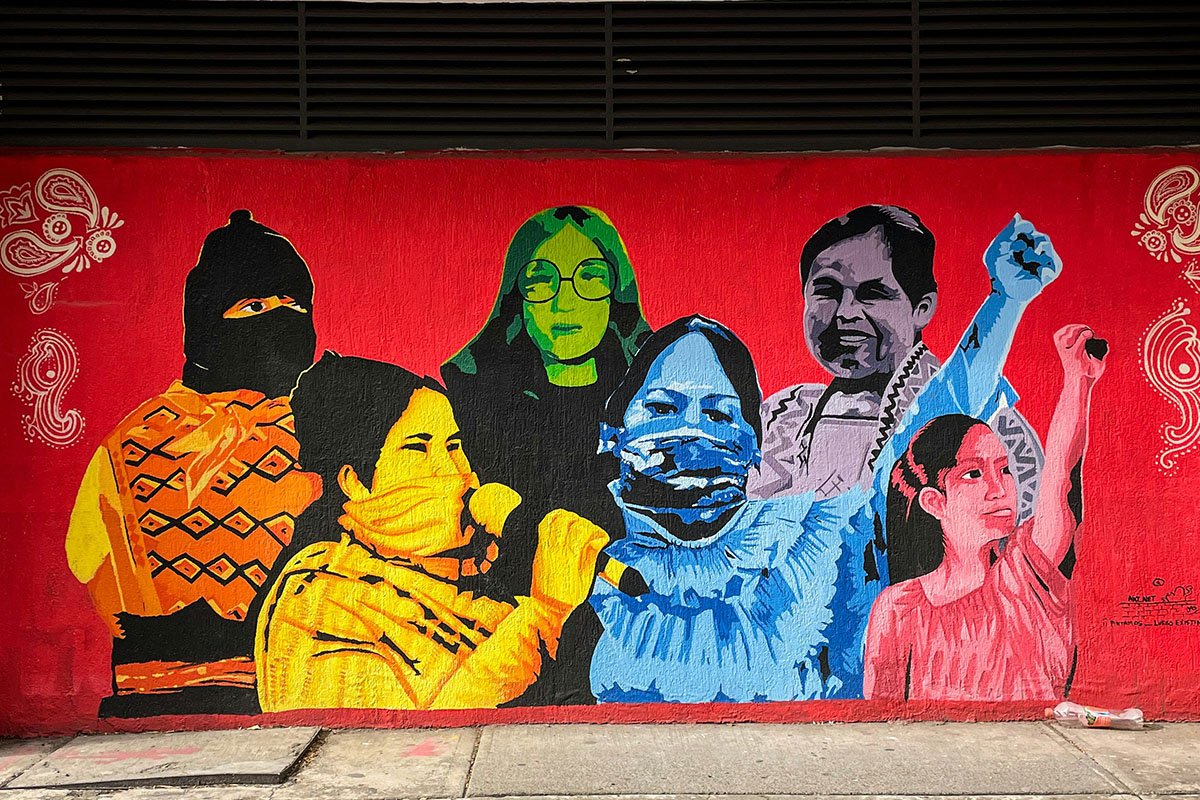 A colorful mural depicting various Mexican woman–young and elder–in various stages of activism. Two have their fists up in protest, one speaks into a microphone, one wears a balaclava, one smiles, and one gazes intensely.