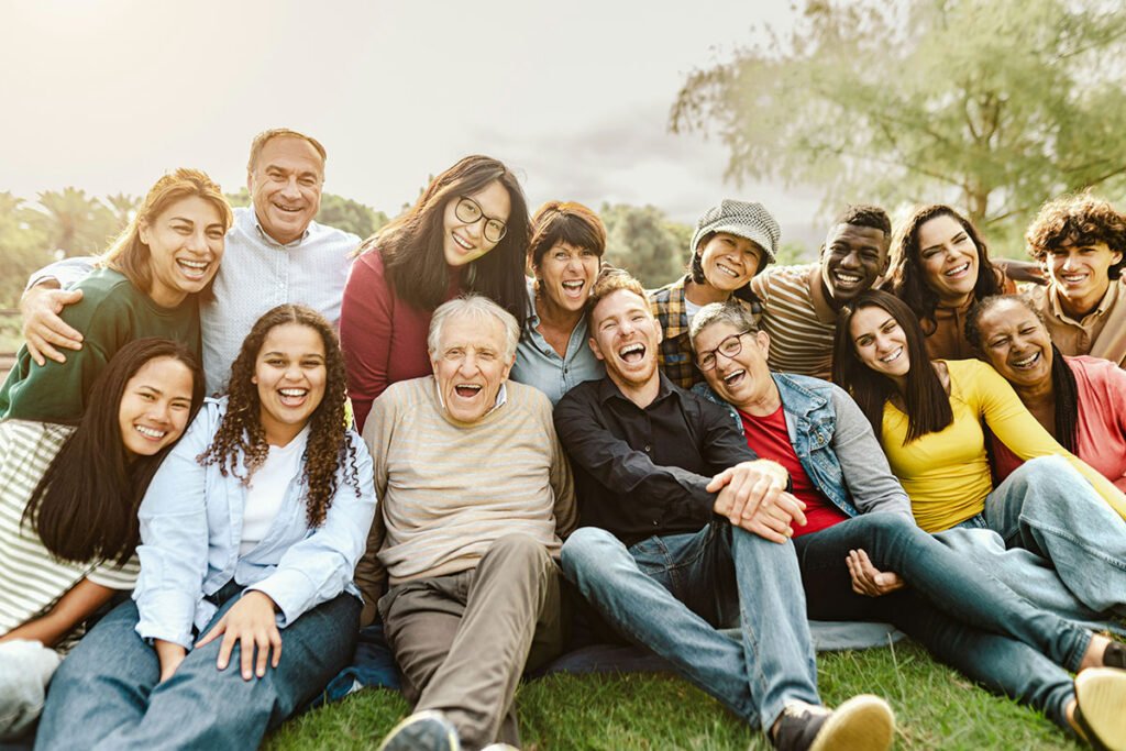 A photo of many people of varying ethnicities and ages, sitting together on the ground and smiling.