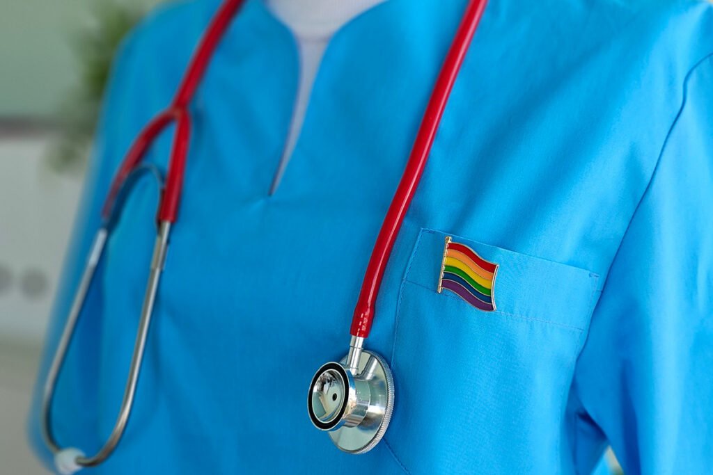 Medical professional in blue scrubs with a rainbow badge and stethoscope around their neck.