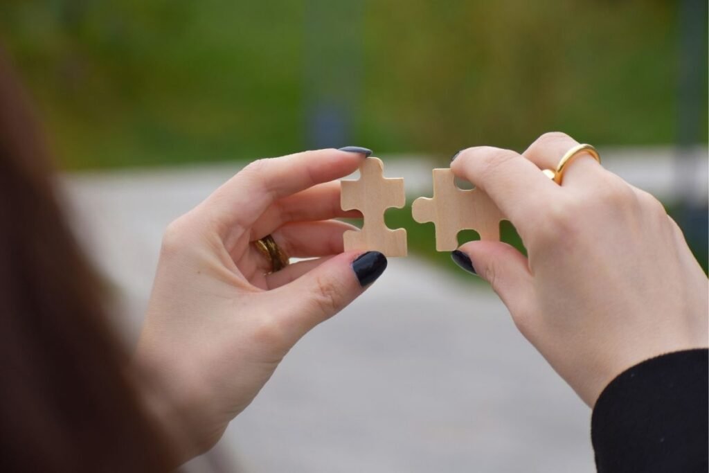 Close-up of two hands holding wooden puzzle pieces and bringing them together against a blurred background.
