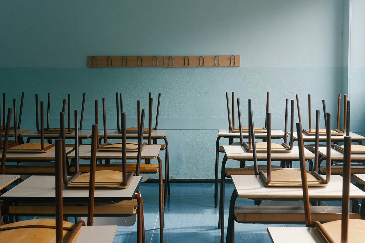 An empty classroom with wooden student chairs stacked on top of wooden desks.
