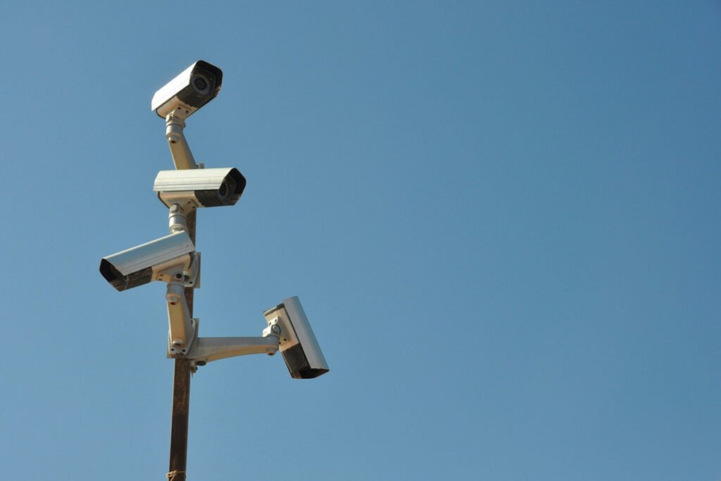 A group of surveillance cameras are mounted in different directions on a single pole against a clear blue sky.